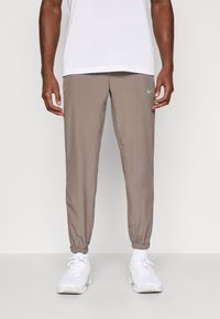 Nike joggingbukser i taupe, lavet af letvægtsstof. Har elastiske manchetter og en lille logo-detalje på venstre lår.