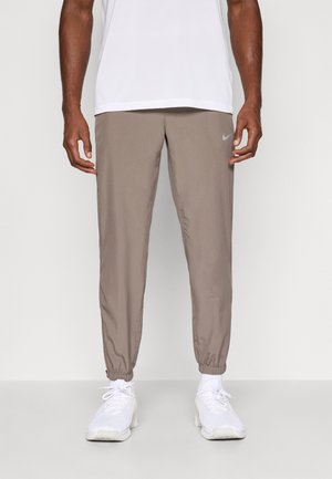 Nike jogger pants in taupe, made from lightweight fabric. Features elastic cuffs and a small logo detail on the left thigh.