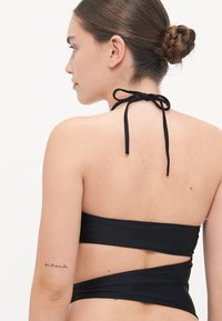 Čierny bikiny top s viazaním za krkom, s obopínajúcim dizajnom a minimálnym pokrytím. Hladká textura, čisté línie a žiadne ďalšie ozdoby.