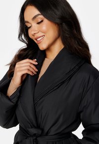 Zwarte puffer-jas met een wikkeldesign, brede kraag en riem. Gladde textuur, geen zichtbare patronen, geschikt voor casual gebruik.