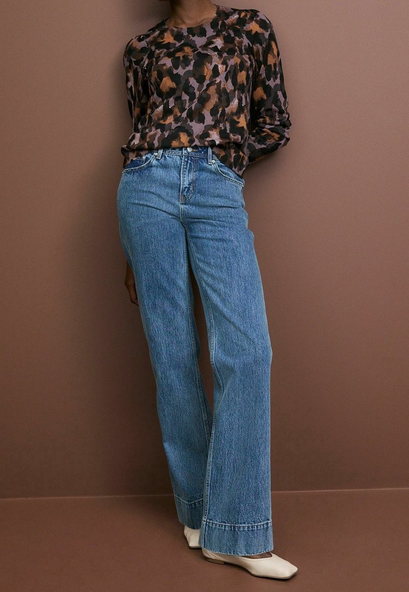 Top a maniche lunghe con stampa leopardata in viola scuro, arancione e beige; abbinato a jeans a vita alta di colore azzurro chiaro, tipo dad, con gambe larghe e orli sfilacciati.