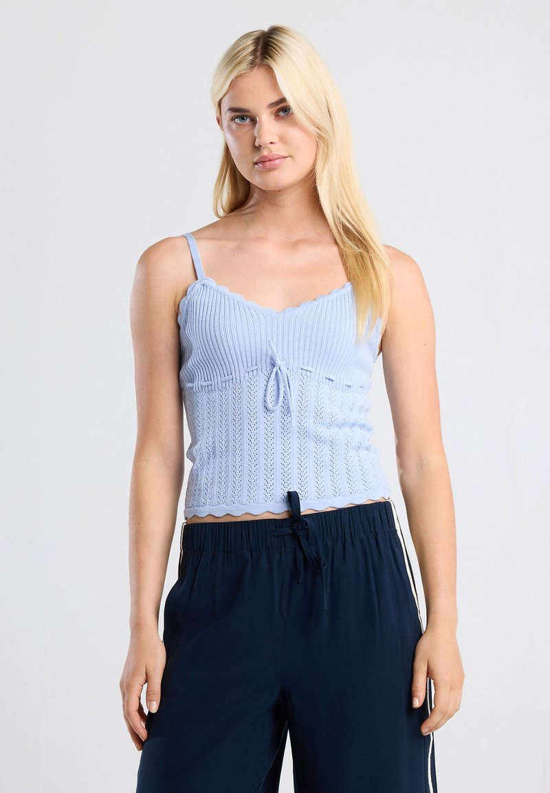 Light blue knitted camisole with scalloped edges and a front tie detail. It features thin straps and a fitted design.