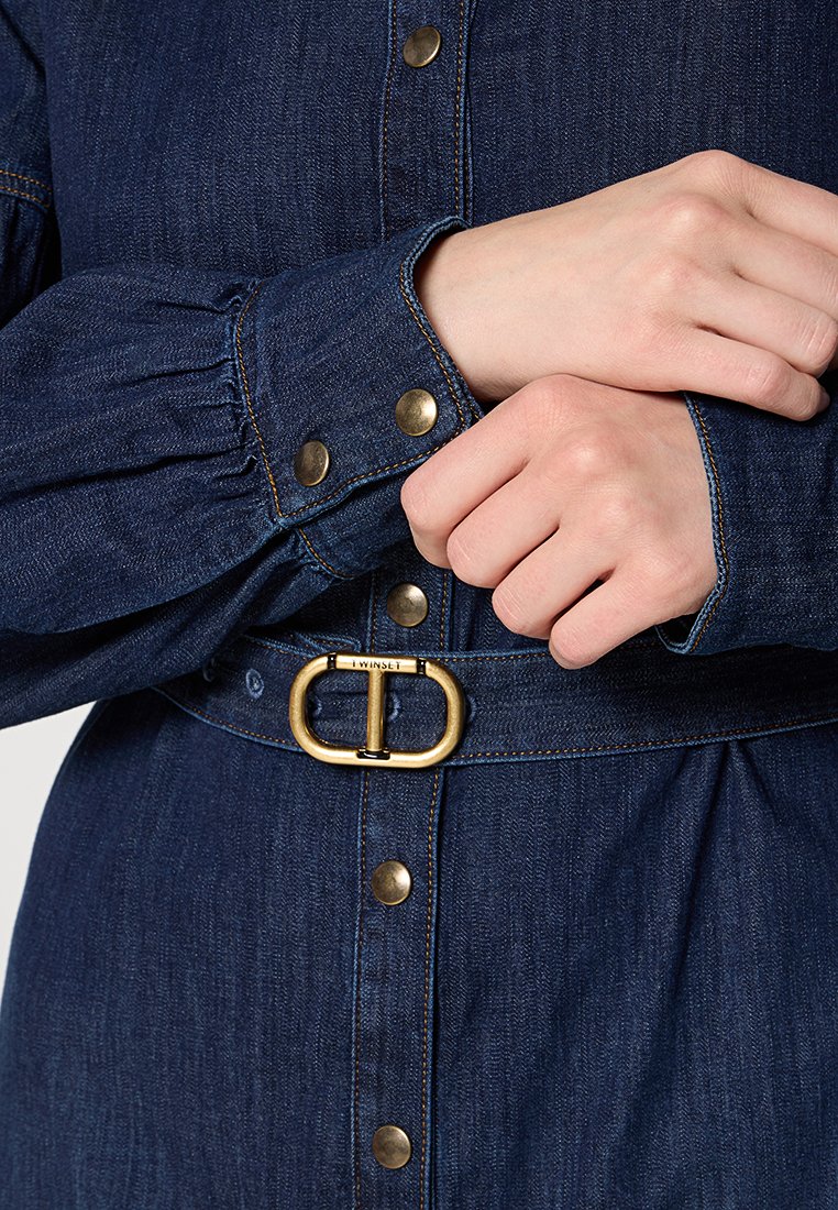 Sukienka koszulowa z dżinsu z dopasowanym pasem, złotym paskiem z metalowymi elementami i zapięciem na guziki z przodu. Posiada bufiaste rękawy i kontrastowe szwy.