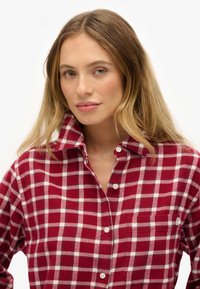 Chemise à manches longues en flanelle à motif carreauté rouge et blanc, avec un devant à boutons et une poche poitrine dotée d'un petit logo. Tissu en coton.