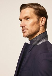 Mornaricnoplavi sako sivi od filca ovratnik, koji se odlikuje glatkom teksturom i detaljima na dugmadima. Dizajn je krojen i strukturiran za oštri izgled.