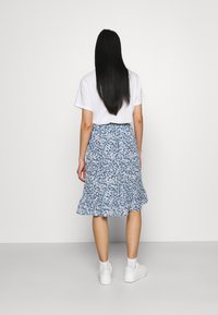 Blommig blå midijupe med volangkant, bärs med en vit t-shirt och vita sneakers. Kjolen har små vita blommor och ett rynkat midjeband.