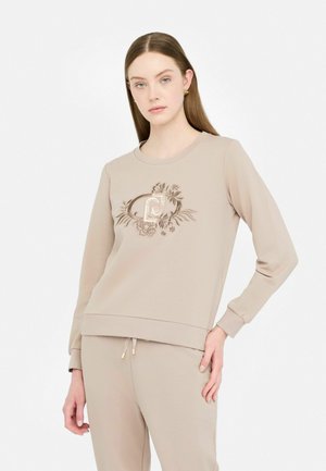 Felpa beige con una texture morbida e un collo a giro, caratterizzata da ricami floreali e un logo. Abbinata a pantaloni jogger beige coordinati.