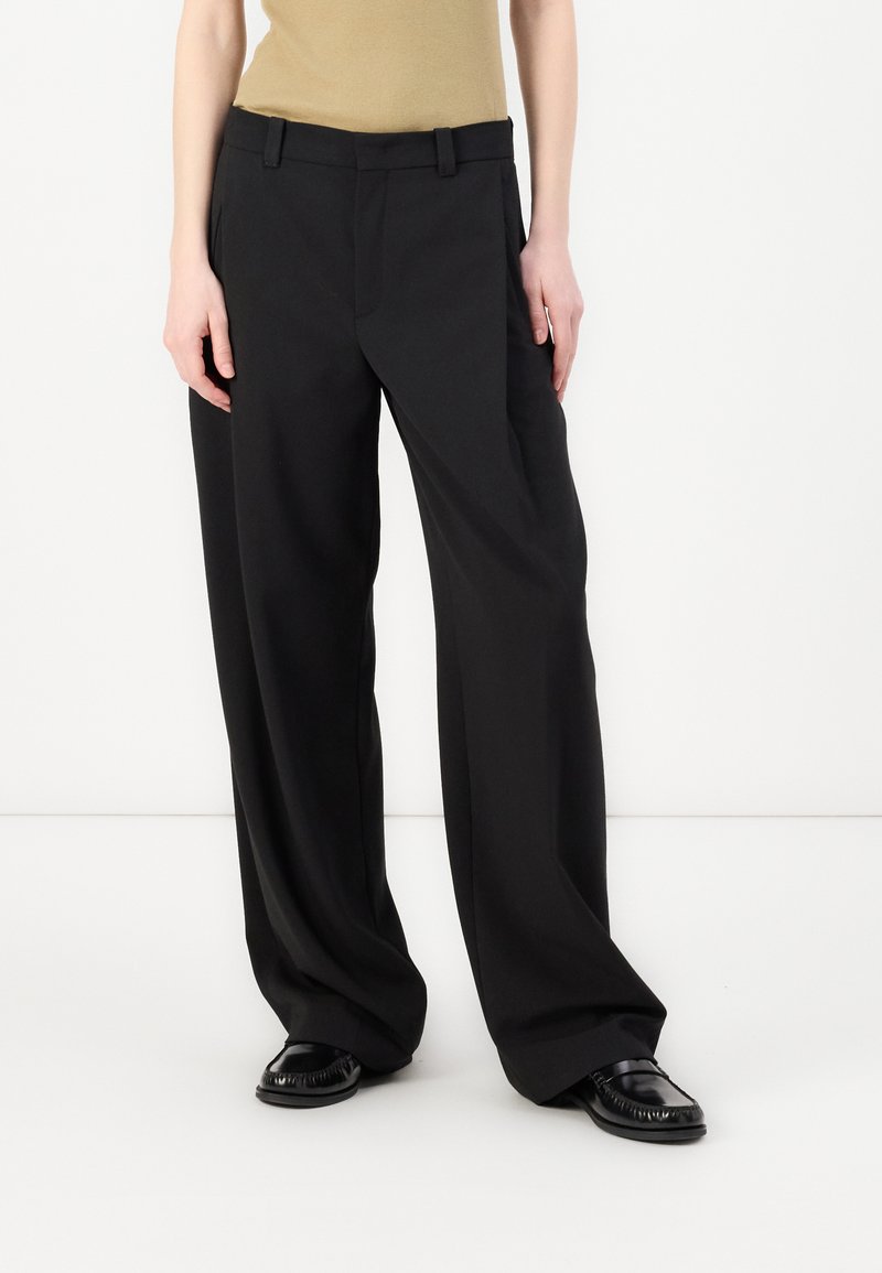 Pantalons larges noirs en tissu lisse, avec un devant plat, des passants de ceinture et des poches latérales pour plus de fonctionnalité.