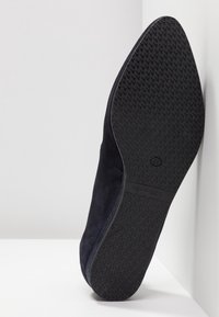 Chaussure en daim bleu marine avec une semelle en caoutchouc noir texturé et un design à bout pointu, mettant en avant une silhouette élégante et épurée.