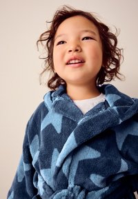 Hætteklæde med blåt og lyseblåt stjernemønster, lavet af blødt plysmateriale med bindebælte og tekstureret overflade.