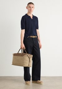 Marineblå kortermet polo, løse svarte bukser, beige duffelbag med brune detaljer, og beige fottøy. Enkel, ren design.