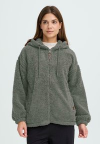 Grüne Fleece-Zip-up-Hoodie mit weicher Textur, einer Kordelzugkapuze und einem dezenten Logo am Saum. Verfügt über weite Ärmel und Fronttaschen.