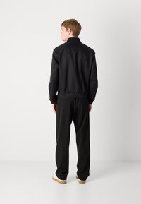 Black bomber jacket with a ribbed collar, elastic waistband, and cuffs, paired with loose black trousers and light-colored shoes.