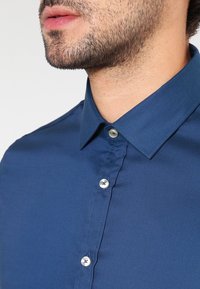 Donkerblauw overhemd met knopen, gemaakt van gladde stof, met een klassieke kraag, zilveren knopen en een nette, op maat gemaakte pasvorm.