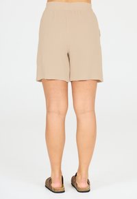 Beige, lätta shorts med elastisk midja. Texturerat tyg, knälång, med en sidoficka. Matcherade med bruna slip-on skor.
