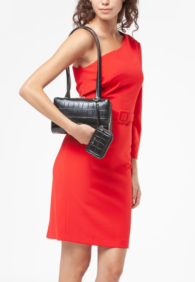 Borsa nera in finta pelle di coccodrillo con due manici, accompagnata da un piccolo portafoglio abbinato, posizionata su un modello che indossa un abito rosso.