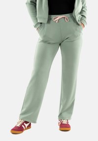 Mintgroene sweatpants met een trekkoord in de taille, zijzakken en een ontspannen pasvorm, gecombineerd met bordeauxrode en crèmekleurige sneakers.