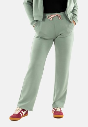 Mintgroene sweatpants met een trekkoord in de taille, zijzakken en een ontspannen pasvorm, gecombineerd met bordeauxrode en crèmekleurige sneakers.
