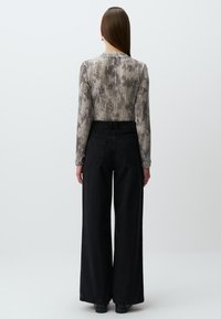 Maglietta a maniche lunghe grigia con motivo a righe verticali abbinata a jeans neri a vita alta con gamba ampia. Tessuto liscio e dettagli classici in denim.
