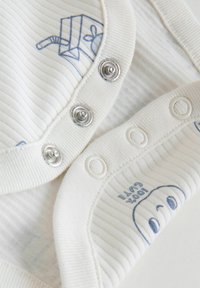 Nærbillede af hvidstribet babybeklædning med trykknapper og blå stregtegning af en juiceæske og et smilende ansigt.