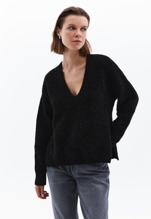 Schwarzer V-Ausschnitt-Pullover aus strukturiertem Strickmaterial, mit langen Ärmeln und lockerer Passform, kombiniert mit grauen Jeans.