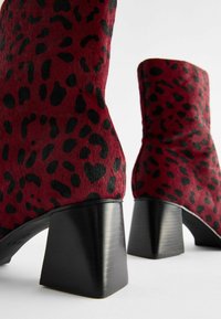 Čizme do članaka crvene i crne boje sa printom leopard uzorka, s teksturiranom završnom obradom, blok potpeticom i glatkim crnim detaljima na dnu.