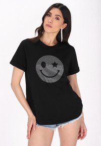 Tricou negru din bumbac, cu un design strălucitor al unei fețe zâmbitoare, însoțit de o stea și un ochi, cu mâneci scurte răsucite și croi lejer.