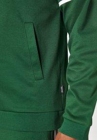 Grüne Sweatshirt aus strukturiertem Stoff mit einer Seitentasche und gerippten Bündchen, mit einem kleinen Etikett am Saum.