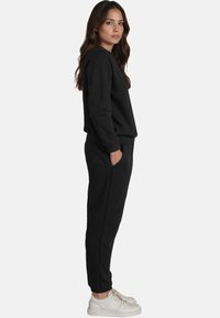 Svart sweatshirt och joggers i mjukt tyg. Har en rundad halsringning, sidfickor och smalnande bendesign. Bärs med vita sneakers.