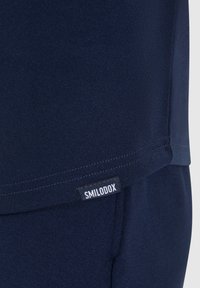 Maglietta sportiva blu navy realizzata in tessuto morbido, con orlo dritto e un piccolo etichetta "SMILODOX" cucita in basso.