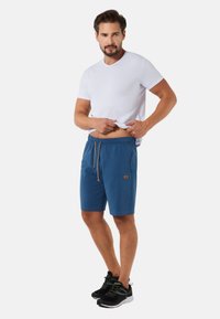 Niebieskie szorty z elastycznym pasem i sznurkiem, z boczną kieszonką i małą naszywką z logo. W połączeniu z białą koszulką i czarnymi sneakersami.