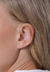 Guld infinity studørering med et strømlinet, minimalistisk design og en glat tekstur, placeret i loben af en models øre.