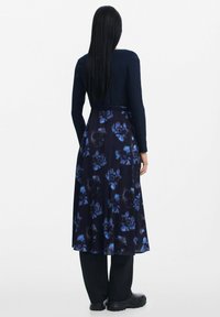 El vestido de manga larga en color marino presenta un estampado floral en tonos azules, una tela fluida y un cuerpo ceñido con una cintura definida.