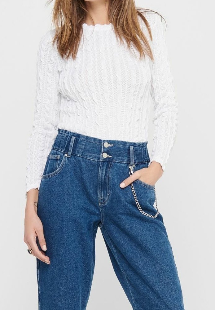 Femme portant un pull blanc en maille torsadée rentré dans un jean bleu taille haute avec un accessoire chaîne argentée sur la poche droite.