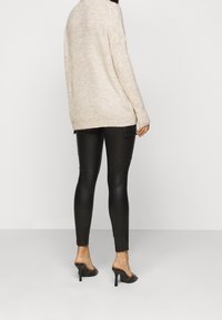 Beige gebreide trui met losse pasvorm en lange mouwen, gecombineerd met strakke zwarte legging van nepleer en zwarte open-toe hakken.