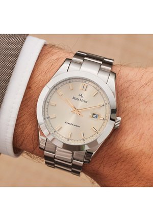 Montre en acier inoxydable argenté avec un cadran beige clair, des index lumineux, un affichage de la date et un bracelet en métal.