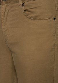 Beżowe bawełniane spodnie o teksturowanej powierzchni, z przednią kieszenią i metalowymi detalami; proste linie, dopasowany krój.