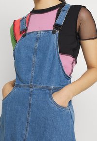 Jeansoveraller i ljusblått med justerbara axelband, framfickor och en avslappnad passform. Har kontrasterande sytt och en mjuk yta.