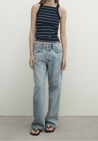Canotta a righe blu navy abbinata a jeans larghi blu chiaro. La canotta ha un design aderente e i jeans presentano una vestibilità rilassata e ariosa.