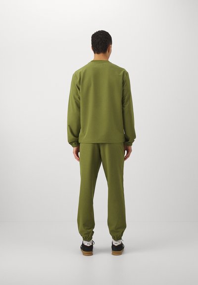 Olivgrüner Jogginganzug aus weichem Material; mit langen Ärmeln, elastischen Bündchen und engen Hosen mit Jogger-Säumen.