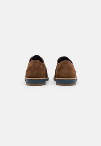 Chaussures en daim marron avec une semelle bicolore. Le talon présente une bande bleue, et le design général est épuré et minimaliste.