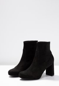 Bottines noires en daim avec un bout arrondi, des panneaux élastiques sur les côtés, et un talon block épais. Texture lisse avec des détails de conception minimalistes.