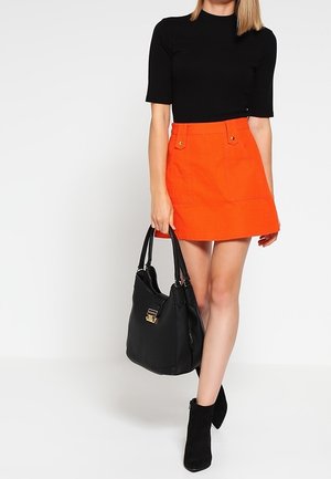 Svart figurnära topp med korta ärmar, orange veckad kjol med framfickor, svart handväska och svarta ankelstövlar. Släta texturer genomgående.