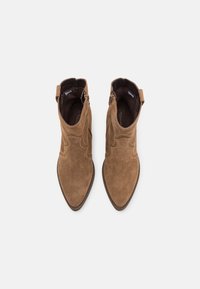 Botines de ante marrón con punta afilada, que presentan costuras decorativas y una cremallera lateral para un uso fácil. Textura suave y tacón bajo apilado.