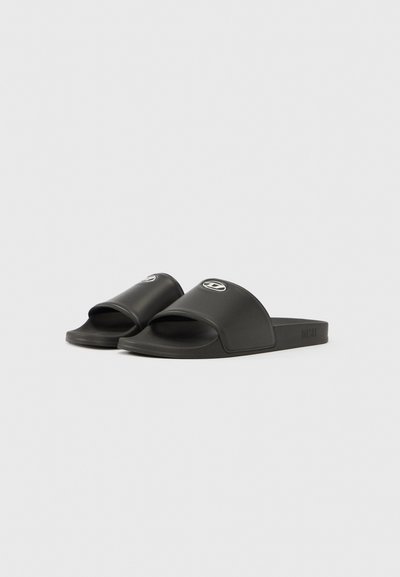 Sandales à glissière en caoutchouc noir avec orteil ouvert et large bride. Présentent un logo estampé en creux sur la bride et une semelle plate pour le confort.