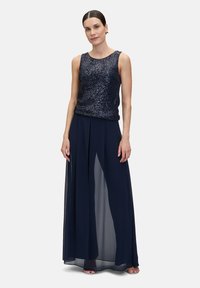 Robe de soirée bleu marine avec un haut sans manches orné de sequins et une jupe fluide et transparente avec des fentes sur les côtés, combinée pour une silhouette élégante.