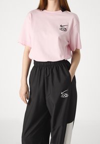 Rosa bomullströja med rund hals och svart Nike-logotyp. Kombinerad med svarta byxor i avslappnad passform med elastisk midja och logodetalj.