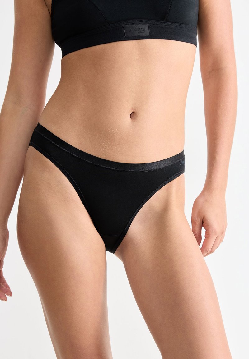 Vrouw in zwarte hoge slip en bijpassende sportbeha, weergegeven van halverwege de dijen tot net onder de borst.