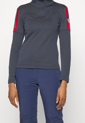 Long-sleeve dark gray pullover with red stripes on upper sleeves and half zipper, worn with navy blue pants.