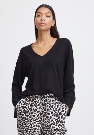 Pull en tricot noir avec un col en V et des manches longues, assorti à un pantalon blanc avec un motif léopard noir.
